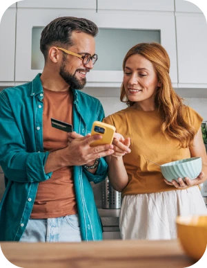 Vīrietis un sieviet stāv virtuvē; vīrietis tur mobilo telefonu un bankas karti, bet sieviete - bļodu. Abi kopā skatās telefonā, it kā veicot pirkumu.