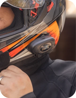 Motocikla ķivere ar piestiprinātu intercom, kas paredzēts sarunu veikšanai un mūzikas klausīšanos brauciena laikā, aizsargķiveres dizains melnā un oranžā krāsā.