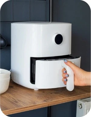 Sieviete ar ziliem nagiem atver baltu aerogrilu, kas novietots uz koka virsmas.