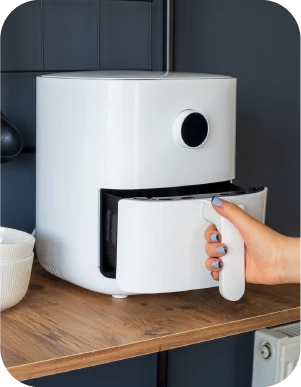 Sieviete ar ziliem nagiem atver baltu aerogrilu, kas novietots uz koka virsmas.