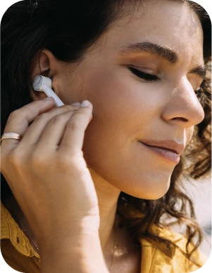 Sieviete ar tumšiem matiem un dzeltenu apģērbu ievieto baltu bezvadu austiņu ausī.