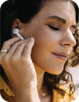 Sieviete ar tumšiem matiem un dzeltenu apģērbu ievieto baltu bezvadu austiņu ausī.