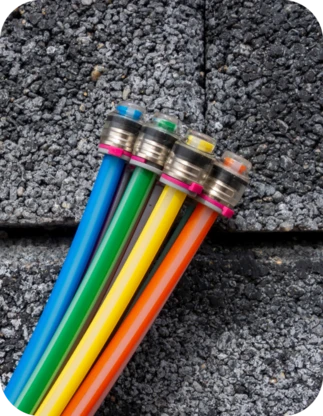 Četri krāsaini kabeļi ar metāla savienotājiem uz pelēka betona fona – zils, zaļš, dzeltens un sarkans vads.