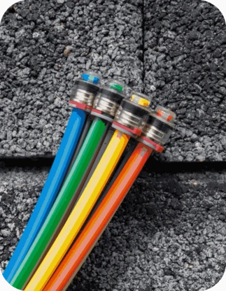 Četri krāsaini kabeļi ar metāla savienotājiem uz pelēka betona fona – zils, zaļš, dzeltens un sarkans vads.