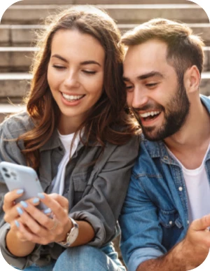 Sieviete un vīrietis ikdienišķā apģērbā sēž uz kāpnēm un skatās mobilajā telefonā.