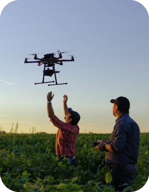 Divi vīrieši stāv laukā, viens vīrietis vada dronu, kas lido virs viņu galvām un otrs vīrietis mēģina satvert dronu.