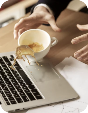 Cilvēks nejauši izlej kafiju uz portatīvā datora tastatūras, mēģinot to apturēt ar rokām; uz galda papīri ar grafikiem.