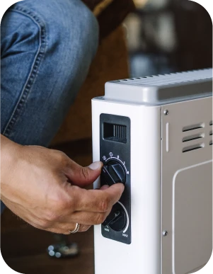 Cilvēks regulē balta elektriskā sildītāja temperatūru, pagriežot vienu no divām vadības pogām.