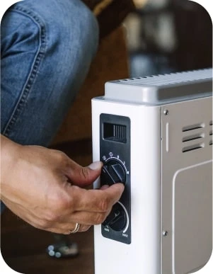 Cilvēks regulē balta elektriskā sildītāja temperatūru, pagriežot vienu no divām vadības pogām.