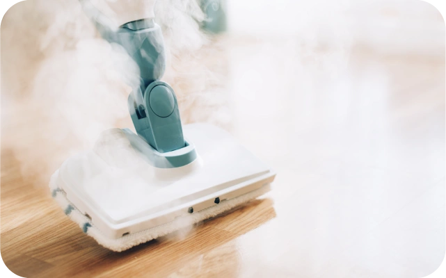 Tvaika putekļu sūcējs ar taisnstūrveida galvu, baltu tīrīšanas lupatu un zilu rokturi, izdala tvaiku uz gaišas koka grīdas.