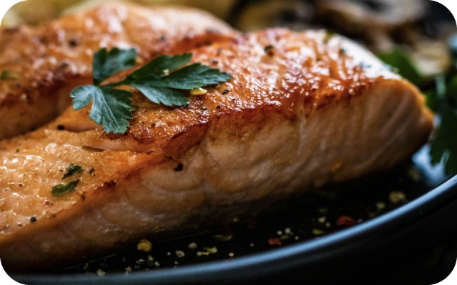 Zeltaini cepta laša fileja uz tumša šķīvja, dekorēta ar svaigām pētersīļu lapām.