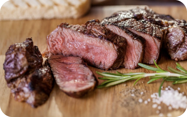 Vidēji cepts steiks uz koka dēļa, dekorēts ar rozmarīna zariņu un apkaisīts ar sāls graudiņiem.