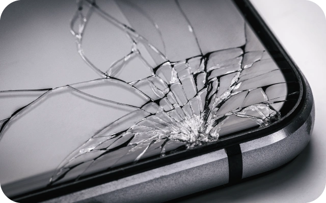 Tuvplāns ar saplīsušu mobilā telefona ekrānu, plaisas izplatās no trieciena vietas apakšējā labajā stūrī.