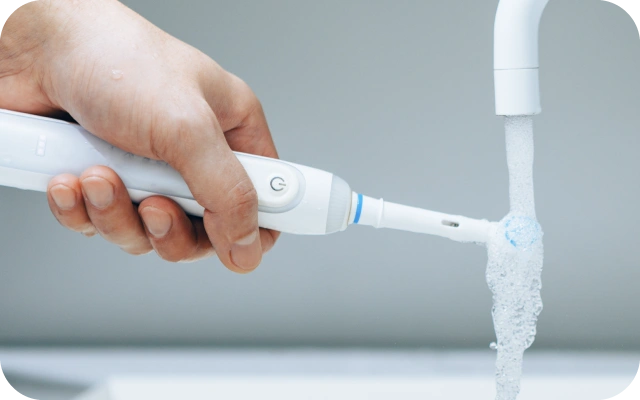 Roka skalo elektrisko zobu birsti zem tekoša ūdens krāna.