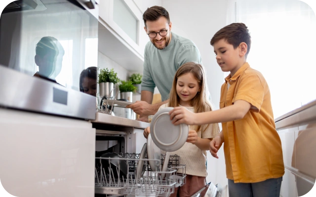 Ģimene, divi bērni un vīrietis, izņem traukus no trauku mazgājamās mašīnas modernā virtuvē.