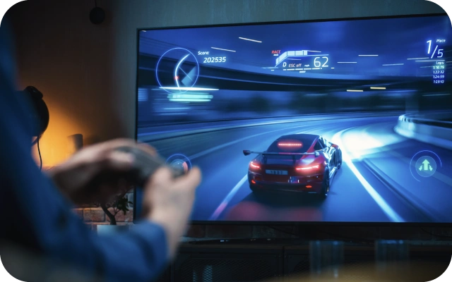 Cilvēks spēlē sacīkšu videospēli, kurā uz televizora ekrāna ir sporta auto uz līkumota ceļa ar spēles rādītājiem, tostarp ātrumu, pozīciju un punktiem.