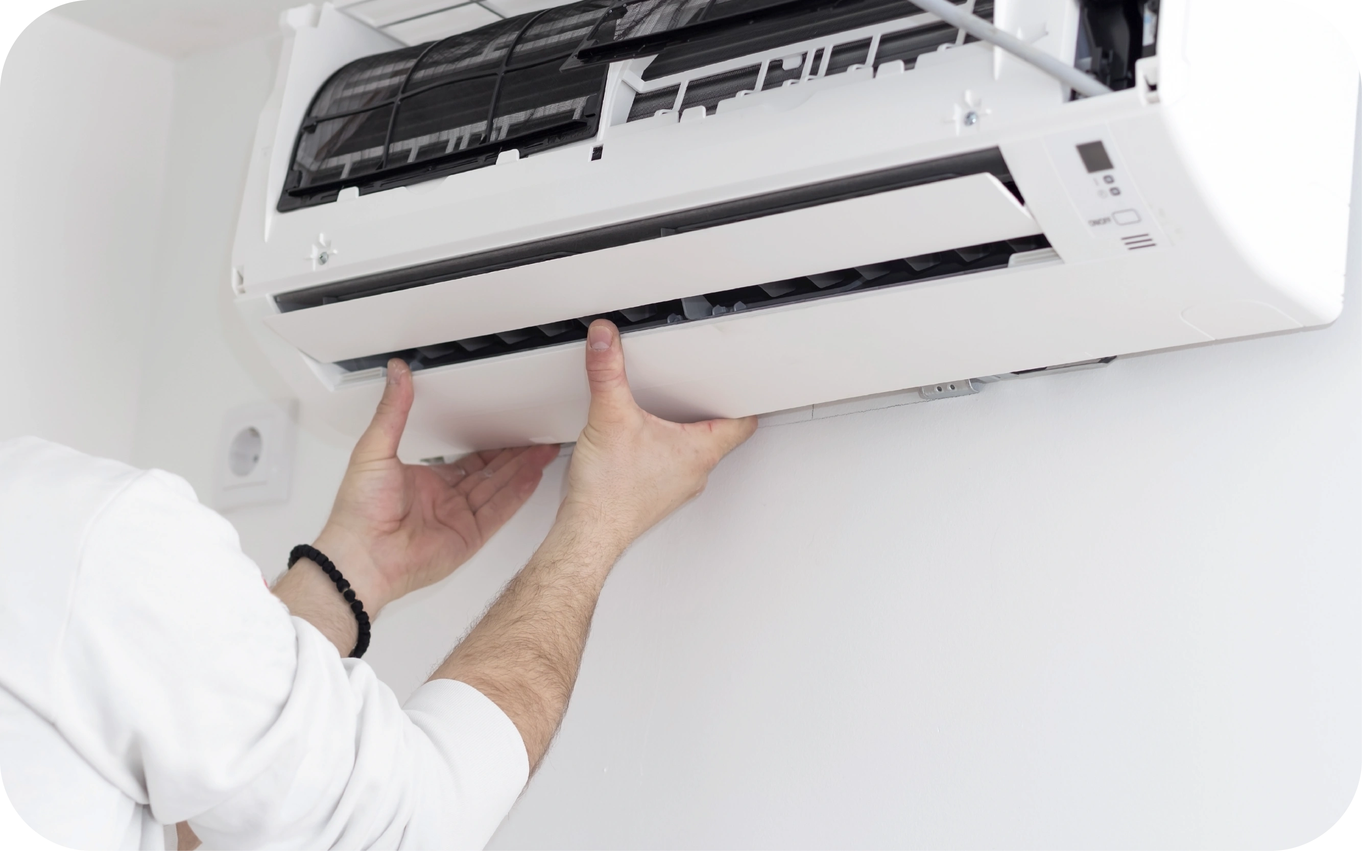 Cilvēks labo vai uzstāda sienas gaisa kondicionieri, turot tā priekšējo paneli.