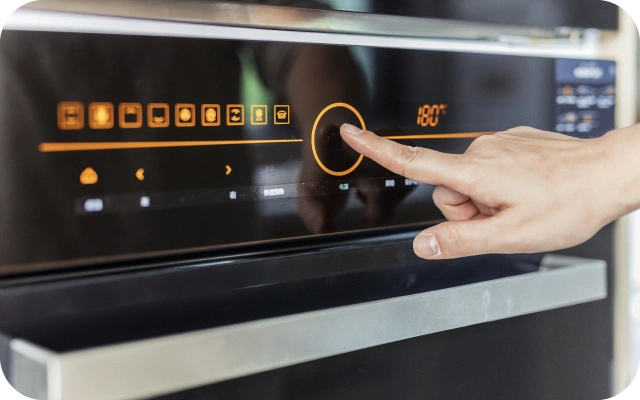 Roka pieskaras cepeškrāsns skārienjutīgajam vadības panelim un iestata 180°C temperatūru un cepšanas programmu