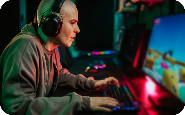 Cilvēks spēlē datorspēles uz jaudīga spēļu datora ar RGB apgaismojumu, spēļu austiņām un mehānisko tastatūru e-sporta un tiešsaistes izklaides vajadzībām.