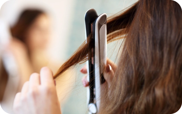 Sieviete taisno matus ar matu taisnotāju, turot pa šķipsnai un izlīdzinot tos.