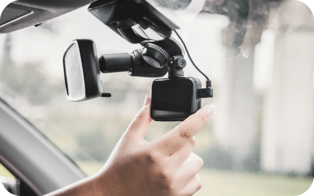 Fokuss uz cilvēka roku, kas regulē videoreģistratora pozīciju automašīnā. Videoreģistrators piestiprināts pie priekšējā stikla.