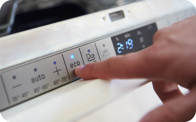 Tuvplāns ar trauku mazgājamās mašīnas vadības paneli; roka nospiež Eco pogu, ekrānā attēlots atlikušais laiks 2:19 min, blakus dažādi ciklu simboli un temperatūras norādes 35°–45°, 45°–65° un 65°–75°.