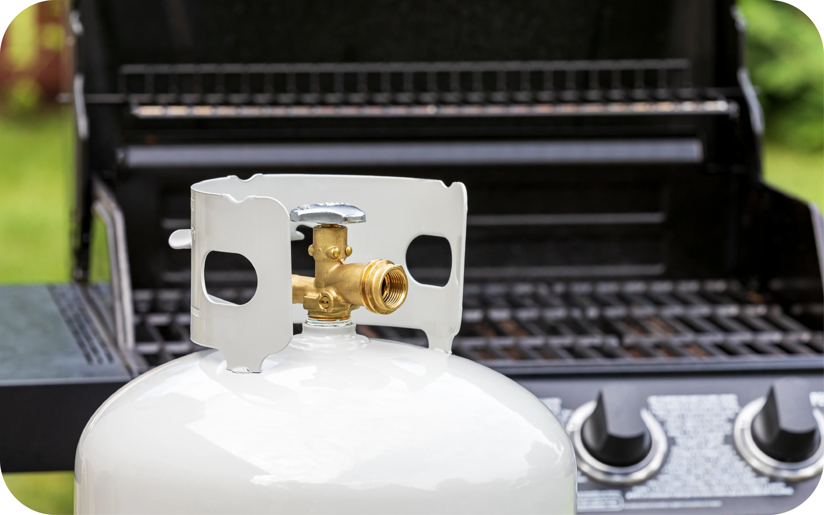 Balsts propāna gāzes balons ar metāla aizsargu un misiņa vārstu novietots pie atvērtas gāzes grila.